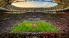 Aerial view of World Cup stadium with illuminated pitch and colorful crowd during golden hour
