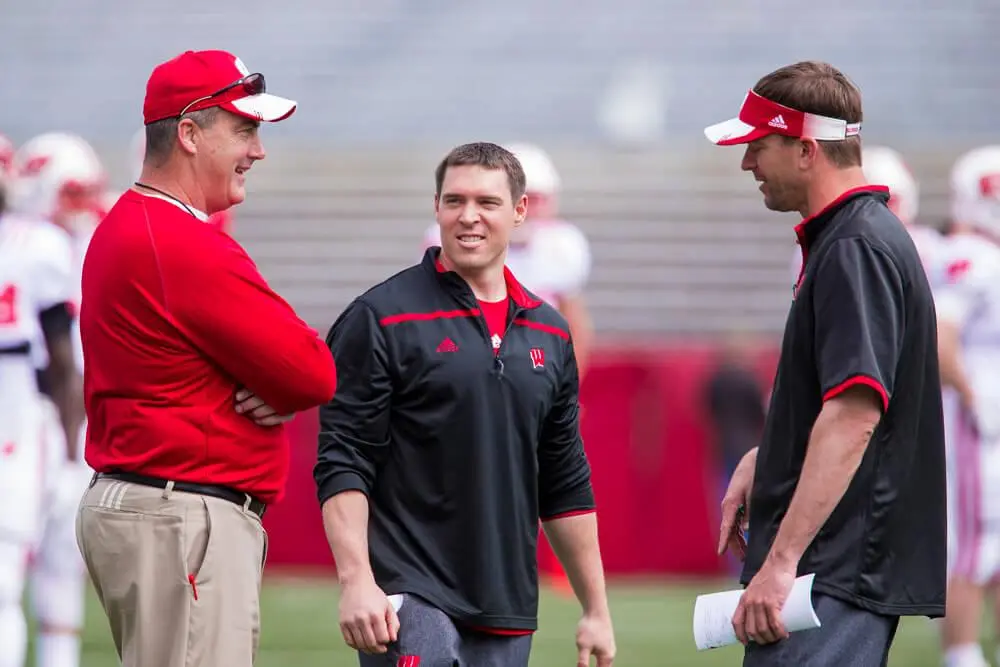 Three football coaches conversing on the field during practice.