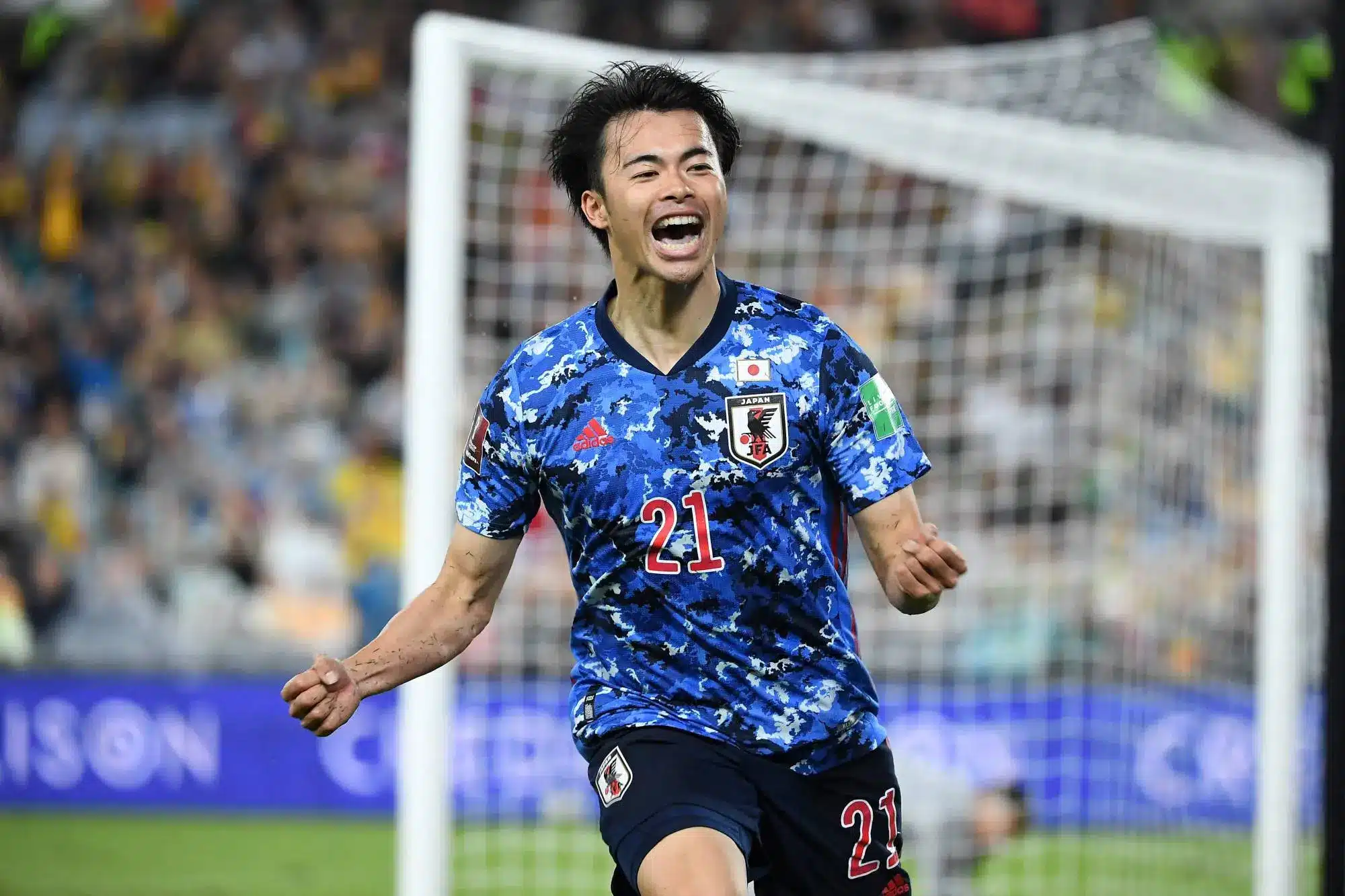 Kaoru Mitoma celebrating a goal for the Japan national soccer team in a blue jersey.