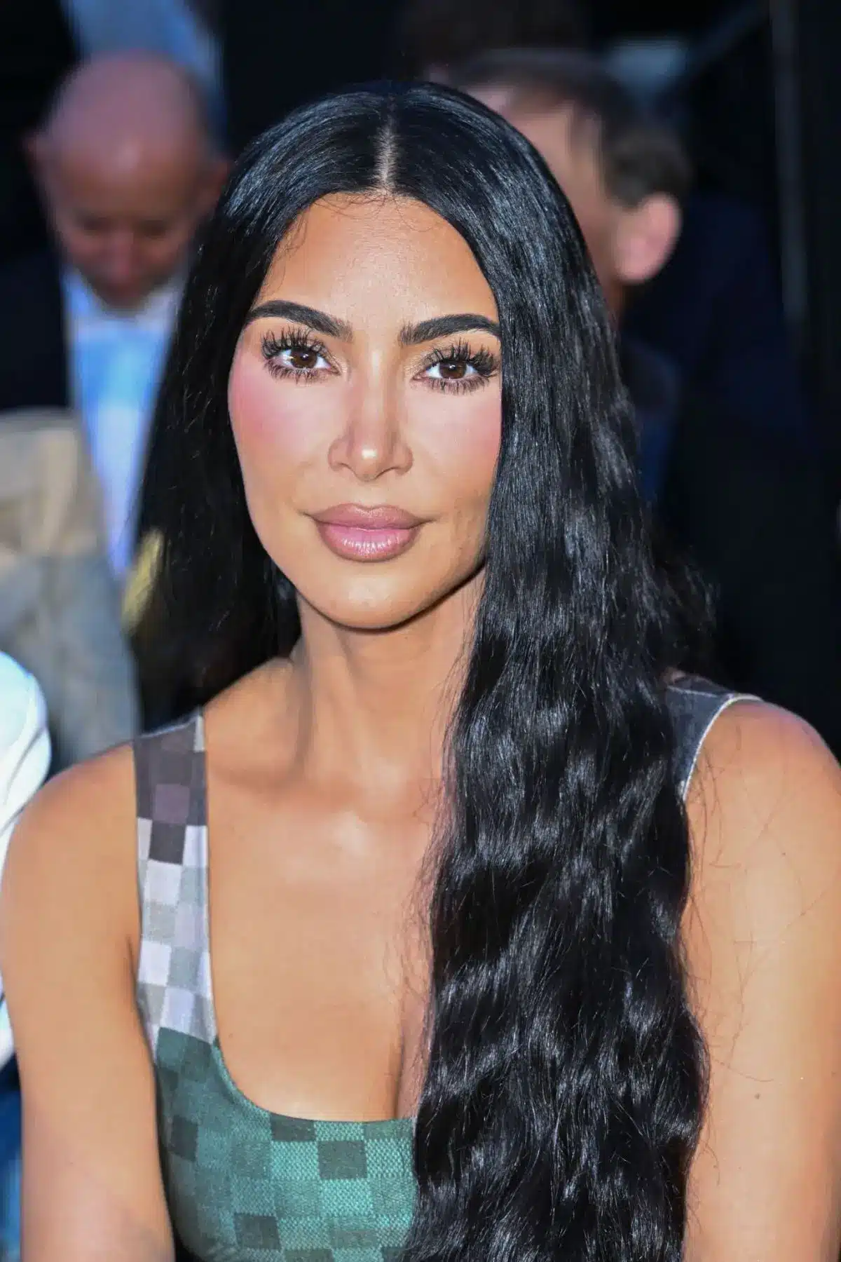 Kim Kardashian seated with long black hair and a patterned dress at an event.