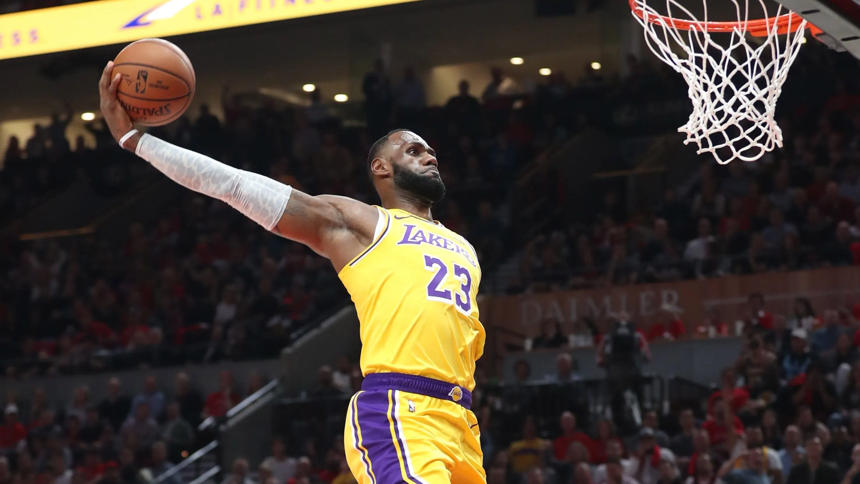 LeBron James in yellow Lakers jersey performing a slam dunk during a game.