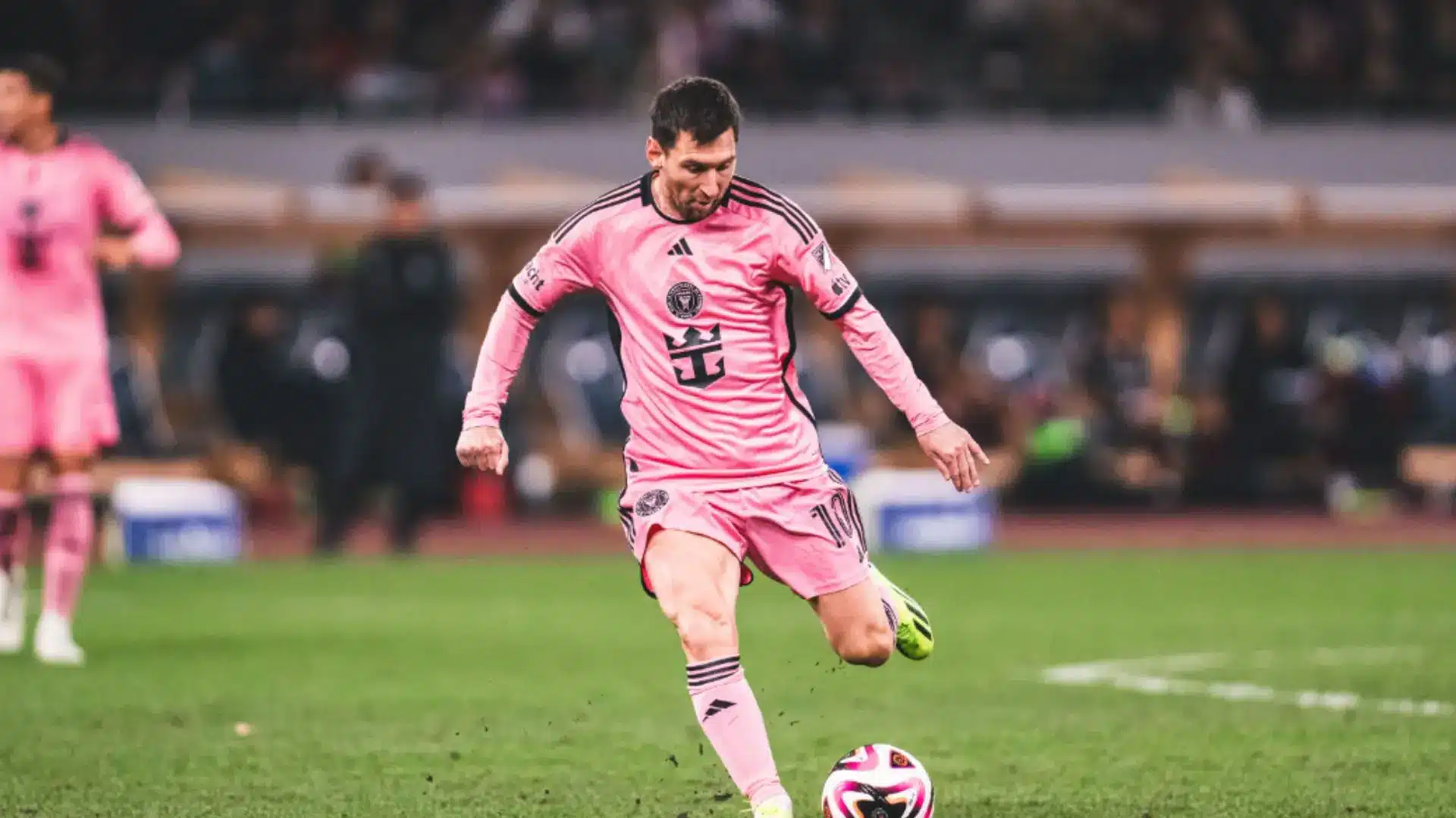 Lionel Messi in a pink Inter Miami FC kit kicking a soccer ball during a match.