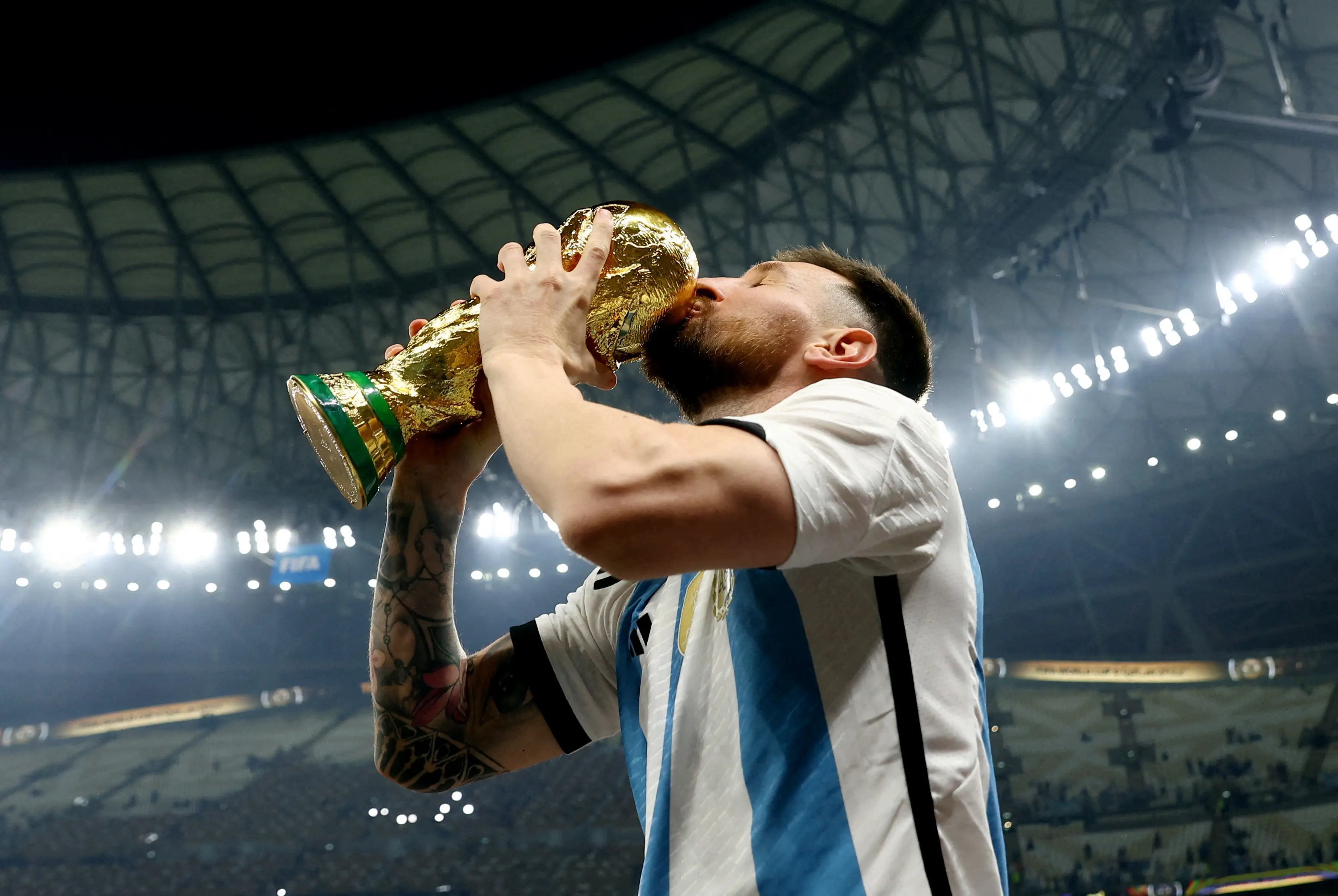Lionel Messi kissing the FIFA World Cup trophy in celebration.