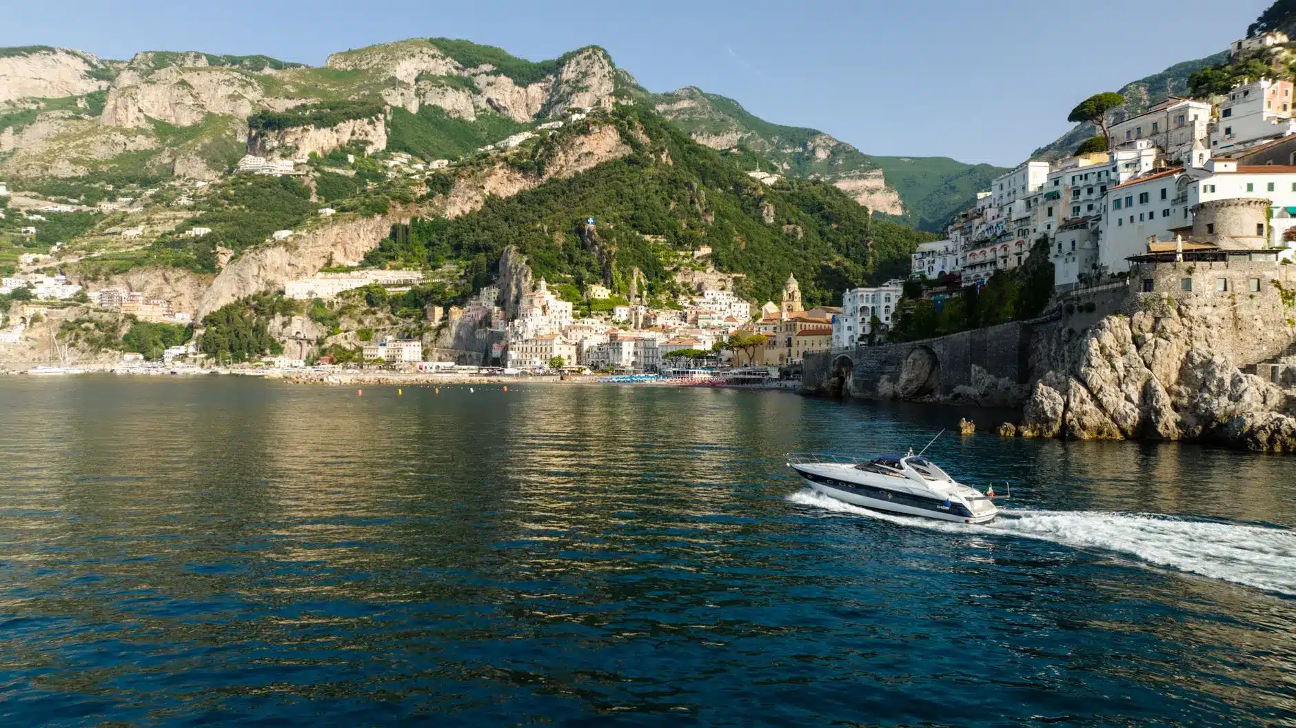 Luxury yacht sailing along the Amalfi Coast with picturesque cliffs and buildings.