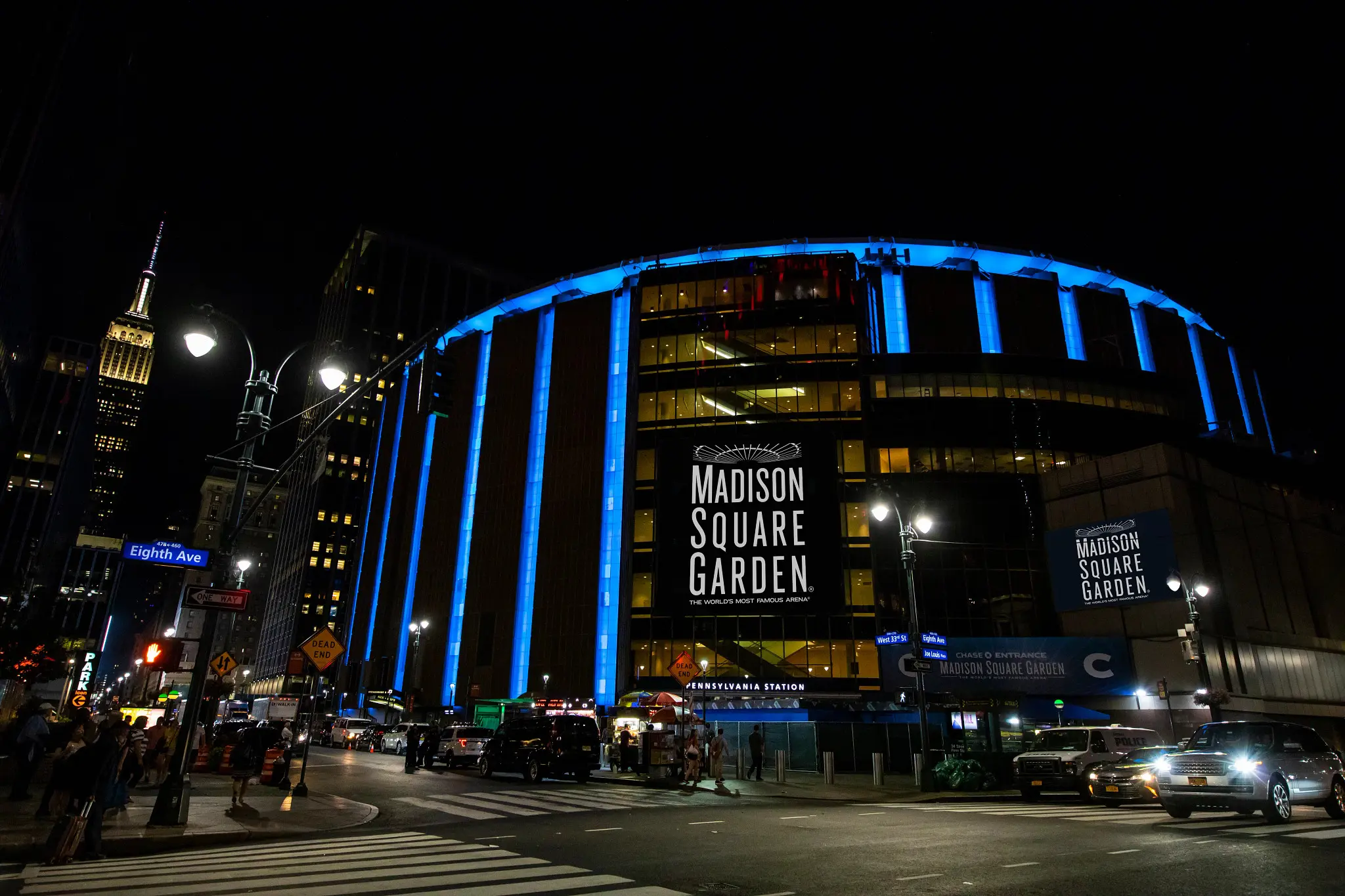 Exterior view of Madison Square Garden at night with blue lights and city skyline.