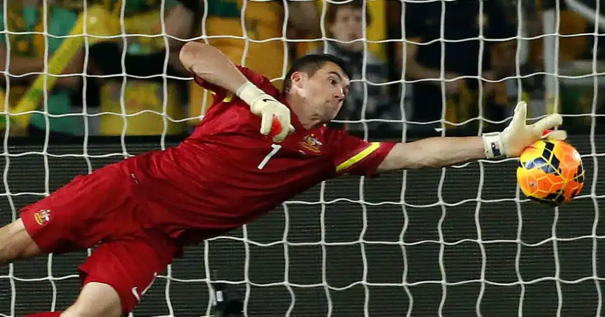 Australian goalkeeper Mat Ryan making a diving save in a red uniform.