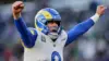 Sean McVay, head coach of the Rams, smiling while holding a play sheet on the sidelines.