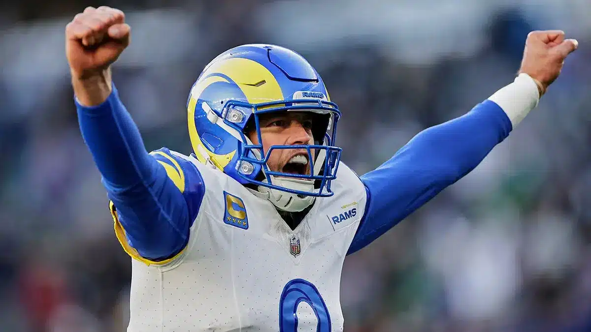 Rams quarterback celebrates with raised arms during a game, wearing a helmet and jersey.