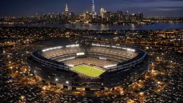Aerial view of illuminated MetLife Stadium at night with New York City skyline in background