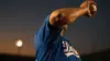 Baseball pitcher mid-delivery in Dodger blue jersey during golden hour at stadium