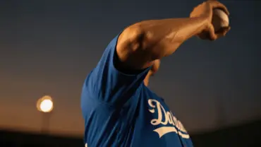 Baseball pitcher mid-delivery in Dodger blue jersey during golden hour at stadium