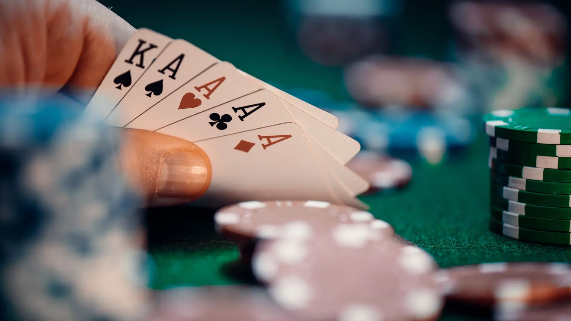 Close-up of a hand holding four aces in a poker game with colorful chips.
