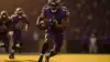 Baltimore Ravens running back exploding through defensive line with football in dynamic action shot