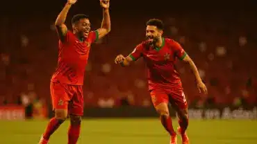 Morocco football players celebrating goal in red jerseys during World Cup match at stadium