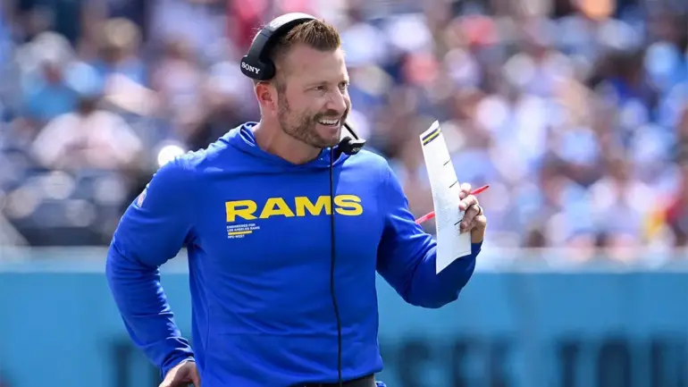 Sean McVay, head coach of the Rams, smiling while holding a play sheet on the sidelines.