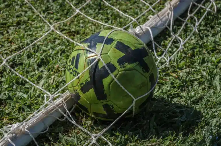 A soccer ball lodged in a goal net on grassy field.