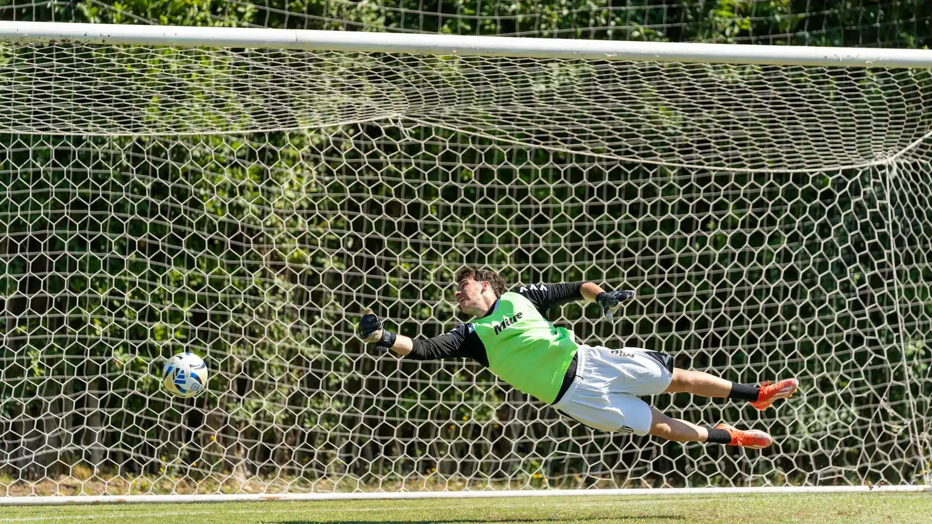 Goalkeeper diving to save a soccer penalty kick with ball in motion.