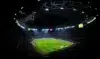 Illuminated soccer stadium at night with players on the field and a cheering crowd.