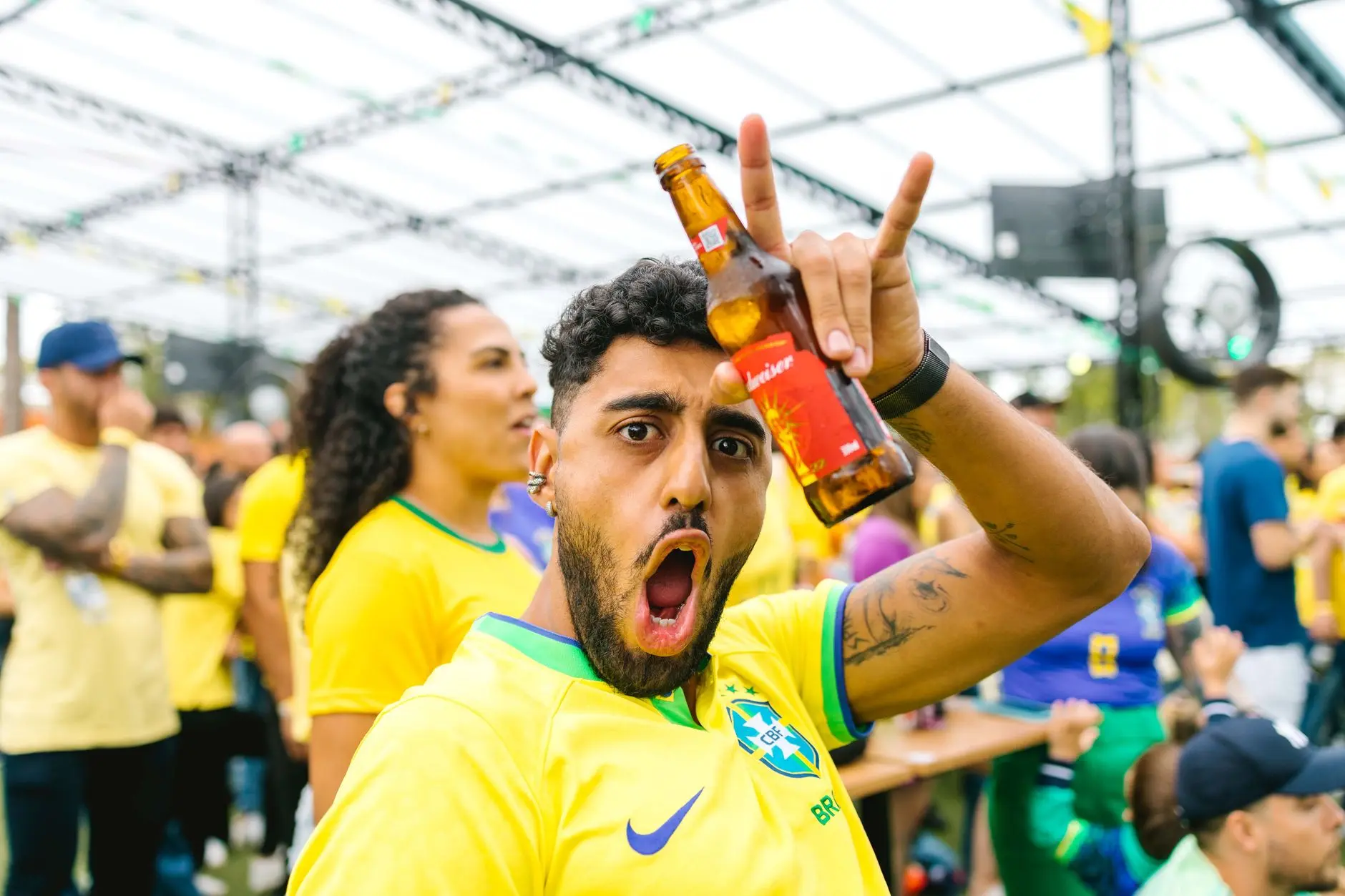 Excited soccer fans in yellow jerseys celebrate at a watch party, holding drinks.