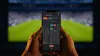 Hands holding smartphone with sports betting app during World Cup soccer match in stadium