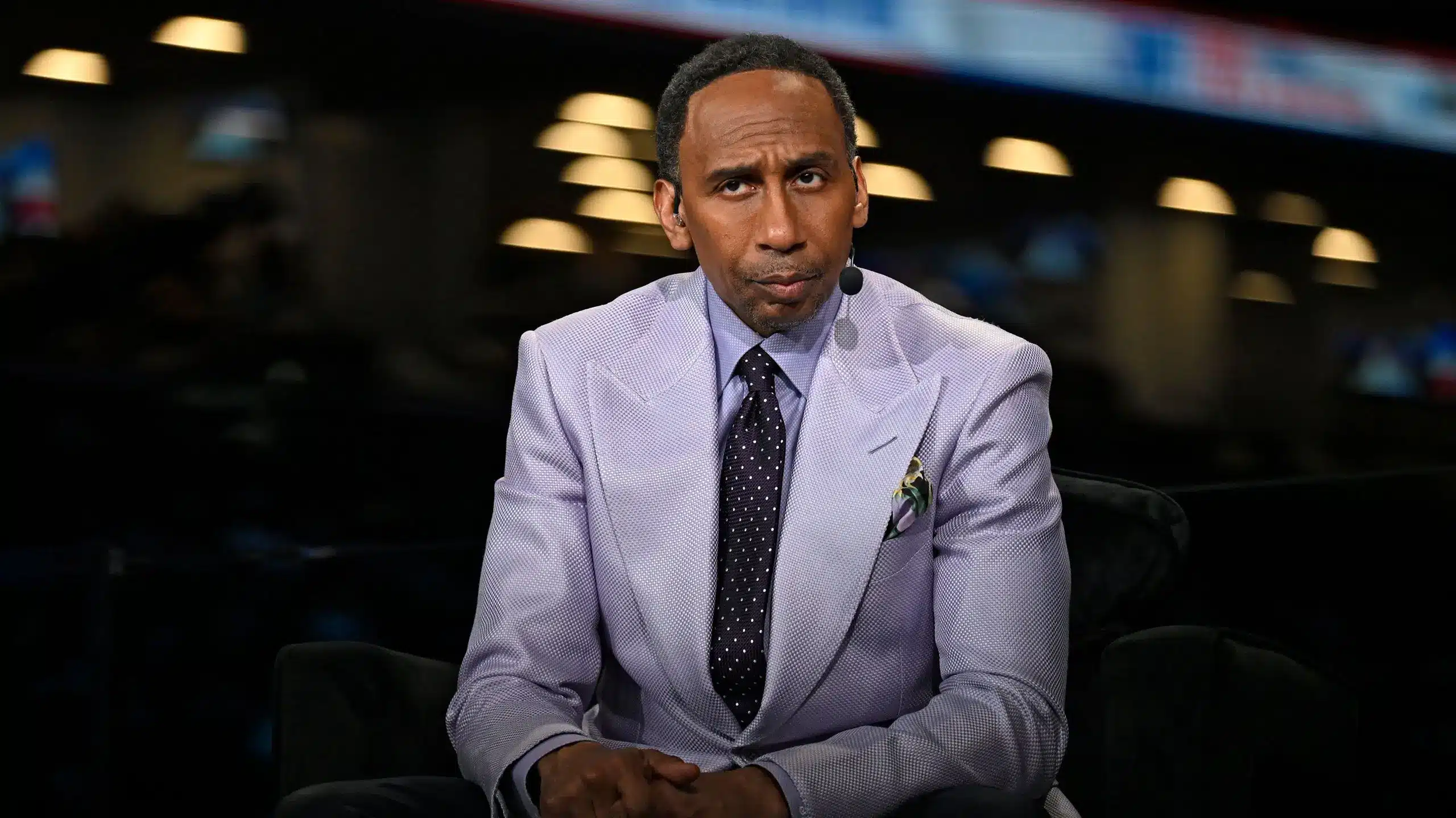 Stephen A. Smith seated at a television studio with microphone.