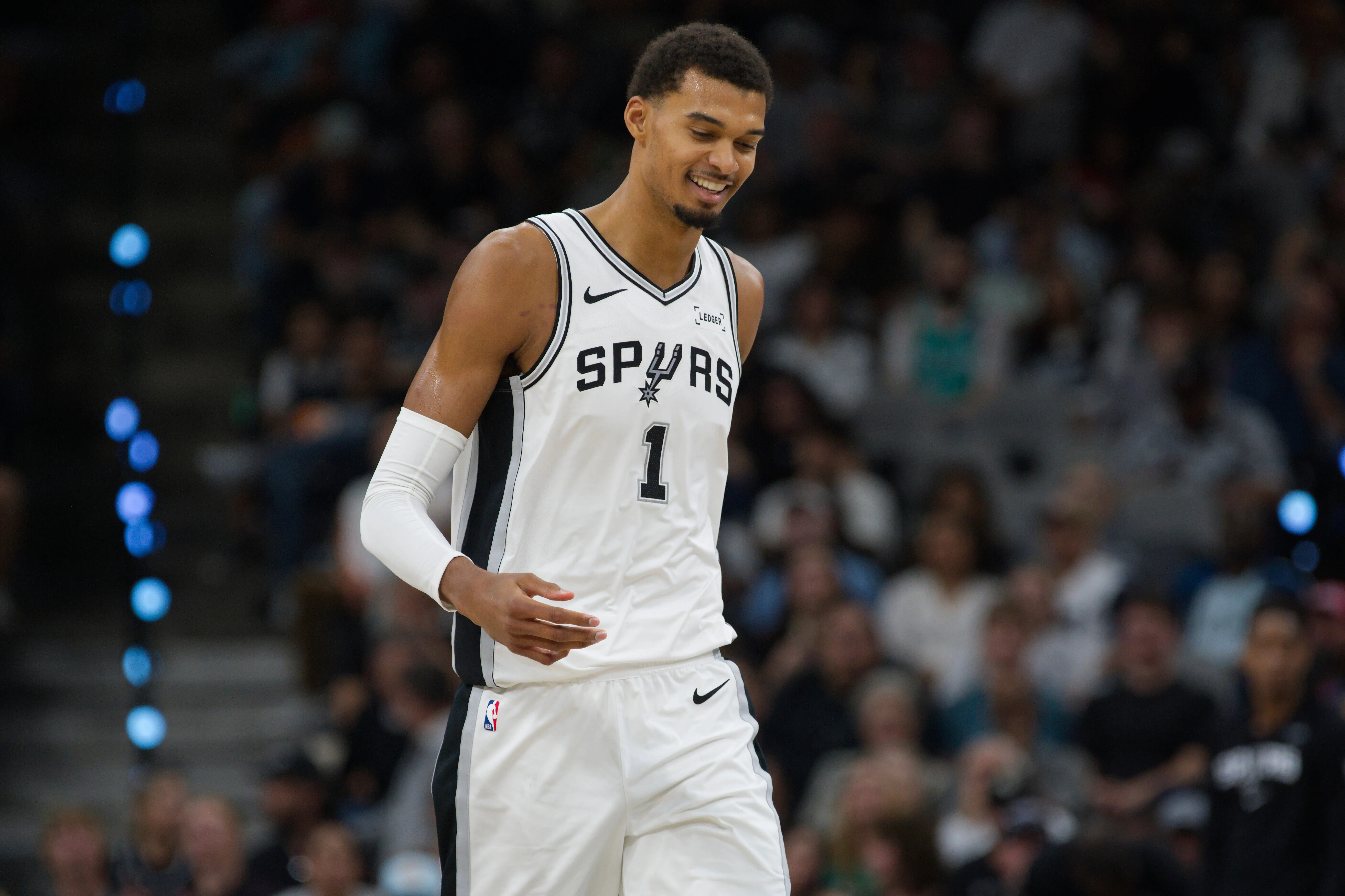 Victor Wembanyama in a San Antonio Spurs jersey smiling on the court during a game.