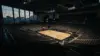 Empty basketball arena interior with dramatic lighting showing vacant seating and hardwood court