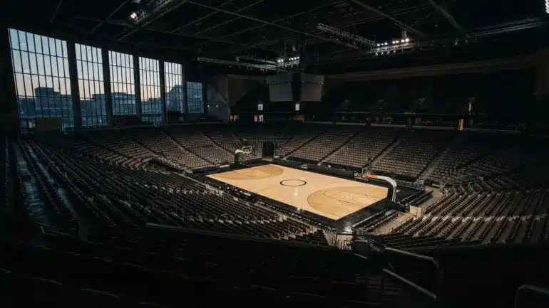 Empty basketball arena interior with dramatic lighting showing vacant seating and hardwood court