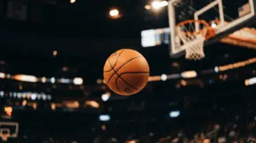 Basketball mid-range jump shot frozen in motion toward NBA hoop with dramatic arena lighting