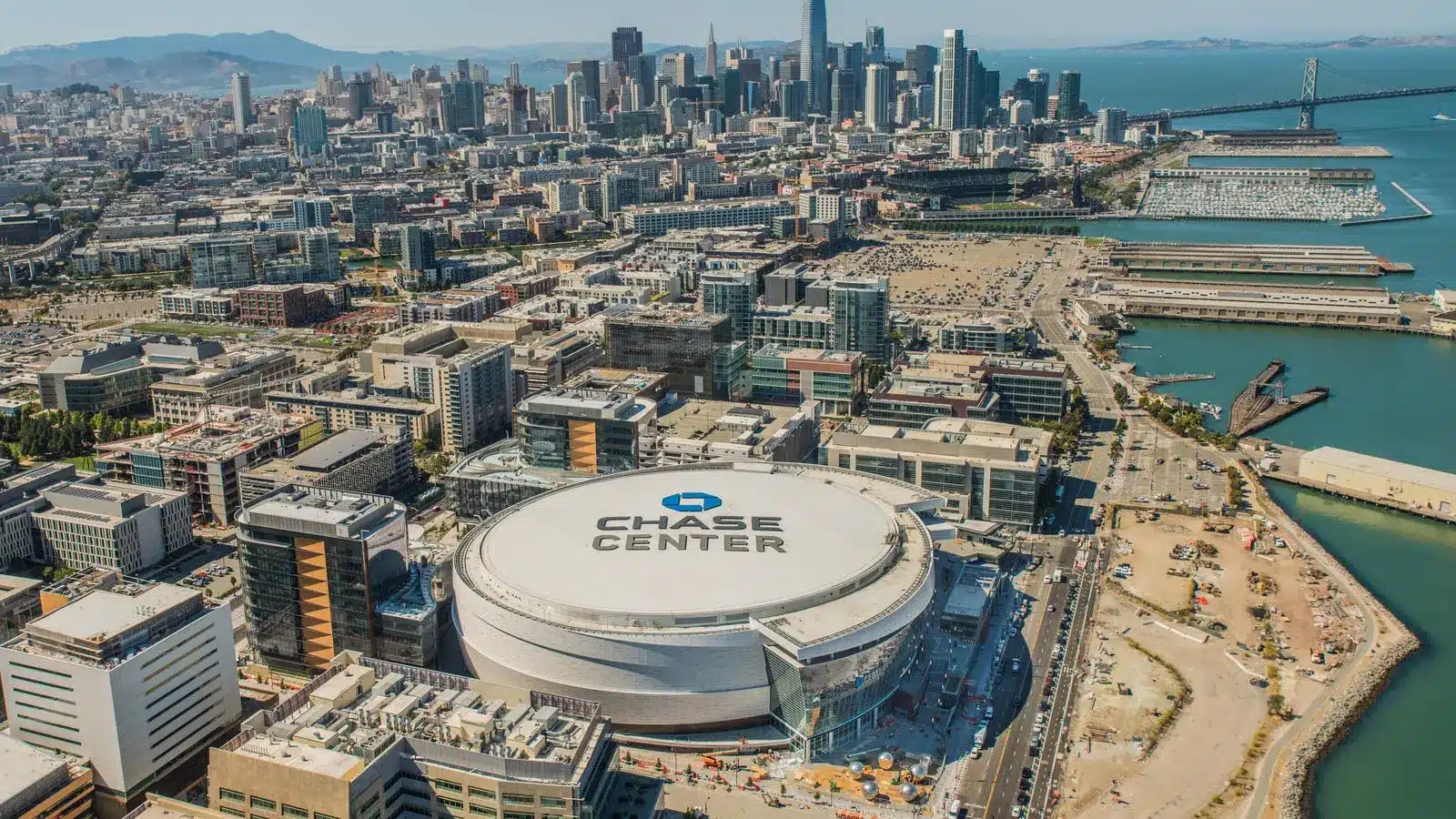 Aerial view of the Chase Center arena in San Francisco with the city skyline and Bay Bridge in the background