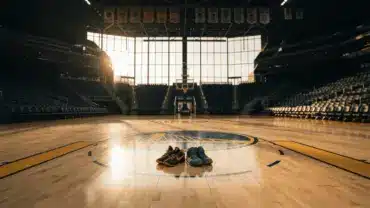 Empty Warriors basketball court with shoes at center court beneath championship banners at golden hour