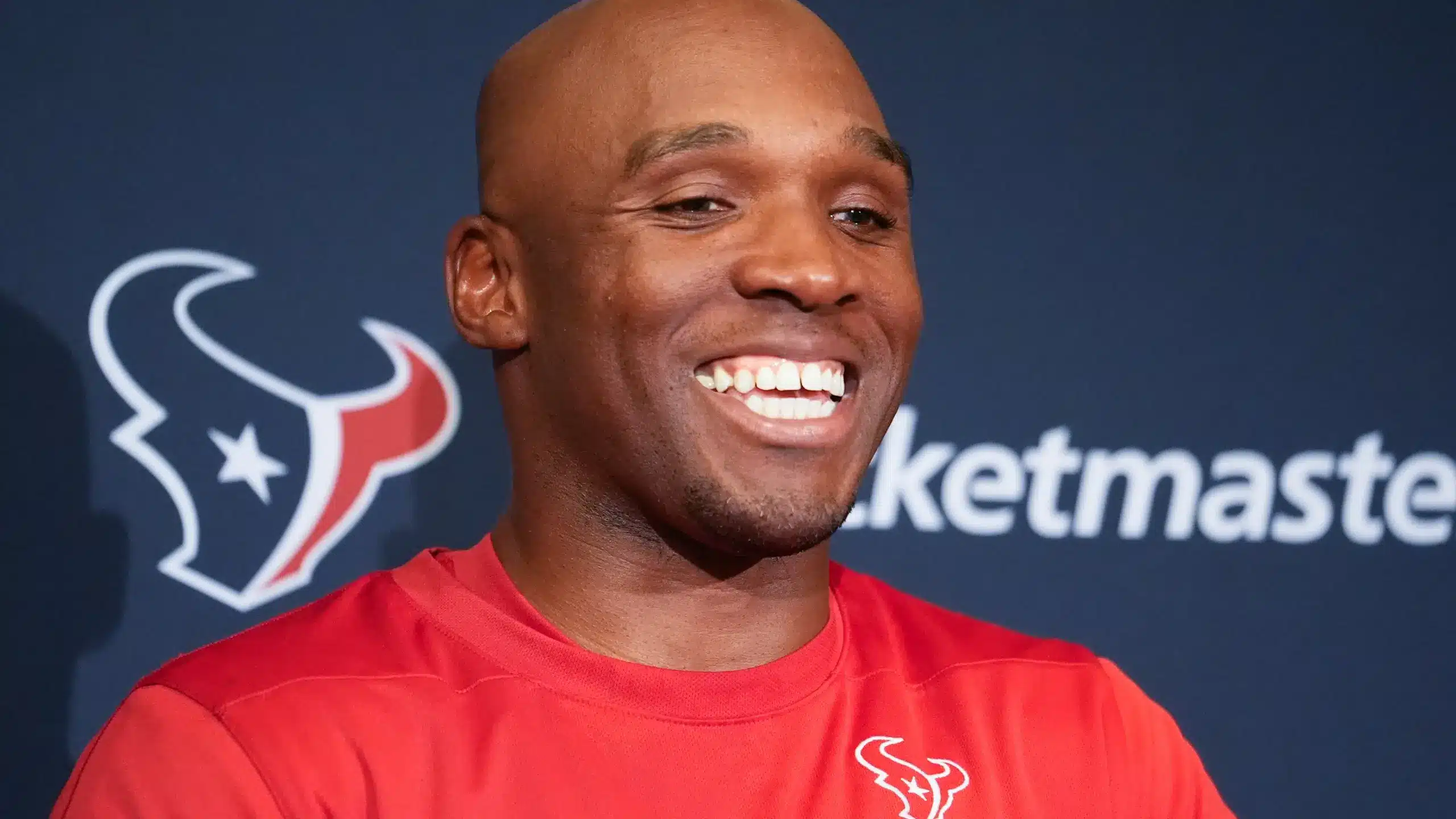 DeMeco Ryans smiling in a red Houston Texans shirt during a media event.