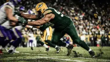 Packers defensive lineman driving through the line in green jersey with dramatic stadium lighting