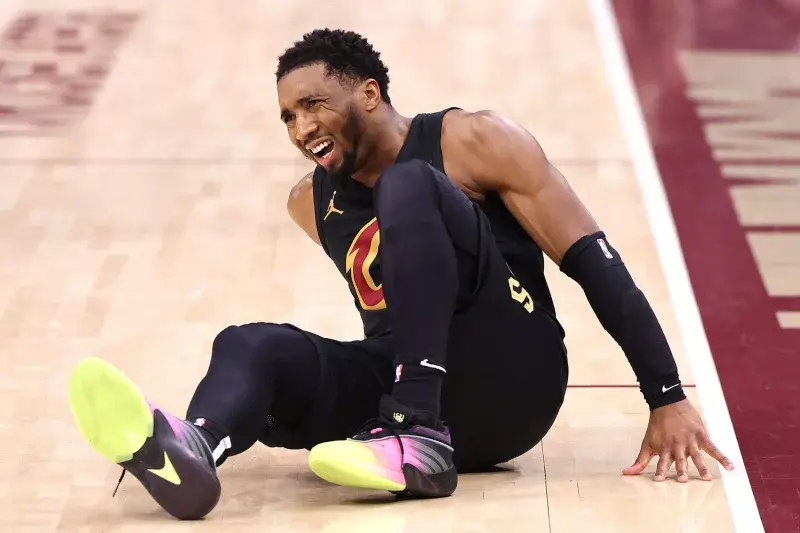 Donovan Mitchell on the court sitting with an injured leg during an NBA game.