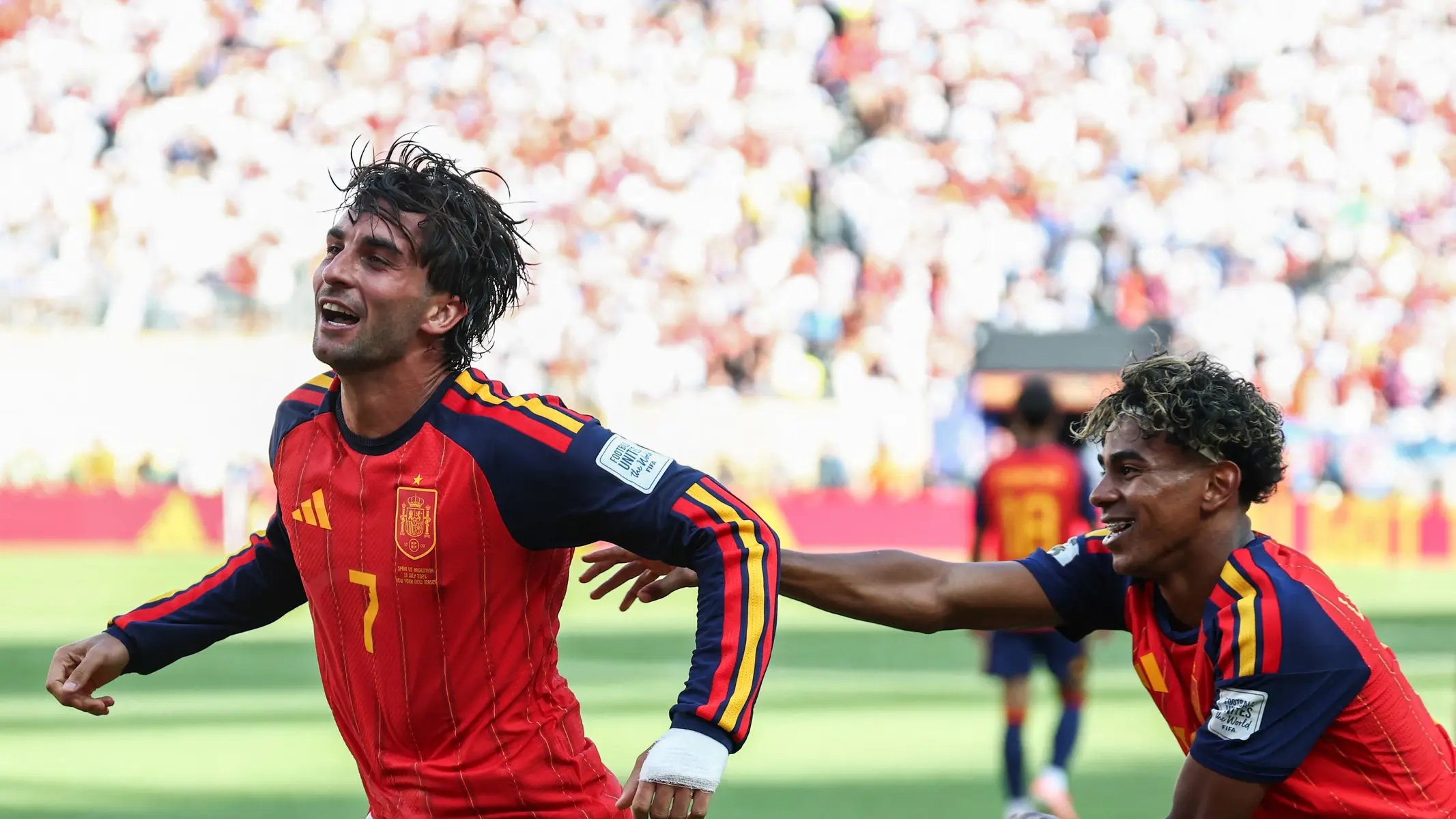 Two soccer players in red Spain jerseys celebrating on the field.