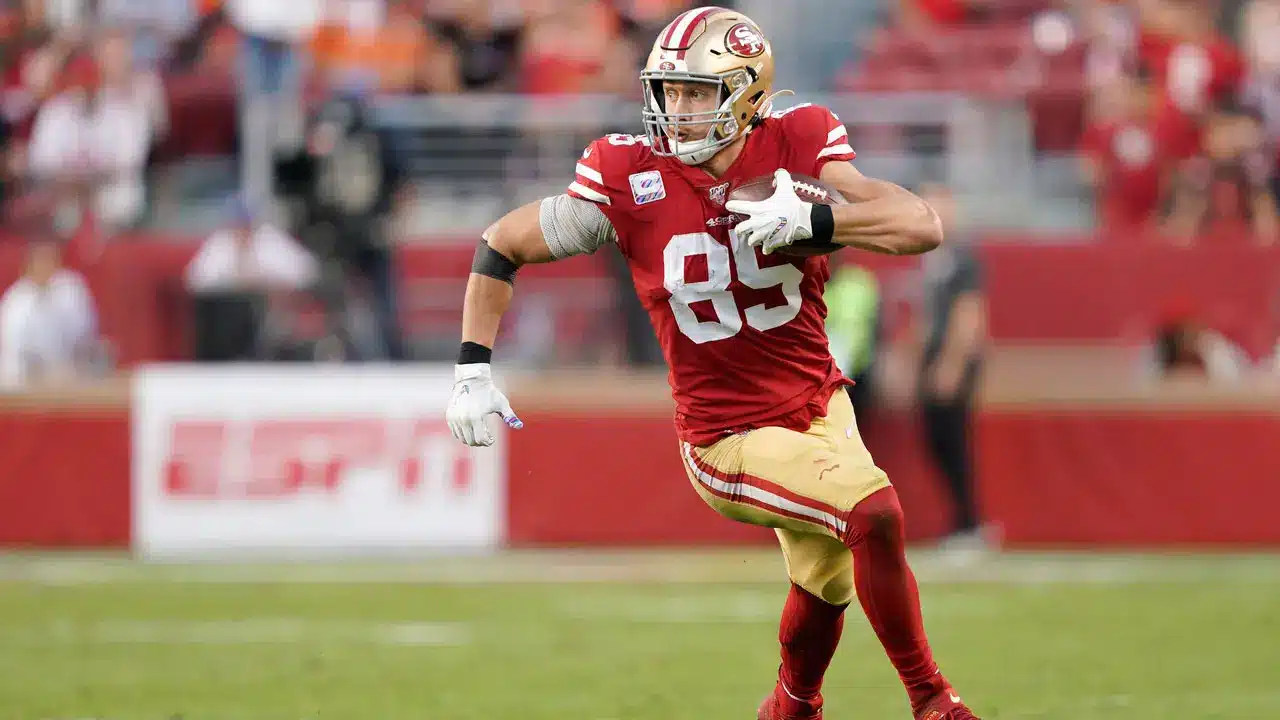 George Kittle running with the ball in a San Francisco 49ers uniform during a game.