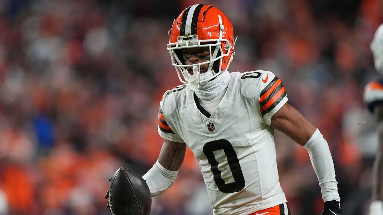 Greg Newsome II in a Cleveland Browns jersey holding a football on the field.