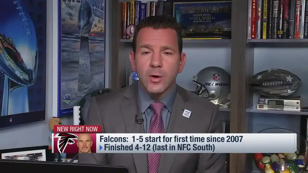 Ian Rapoport reporting NFL news in front of sports memorabilia.