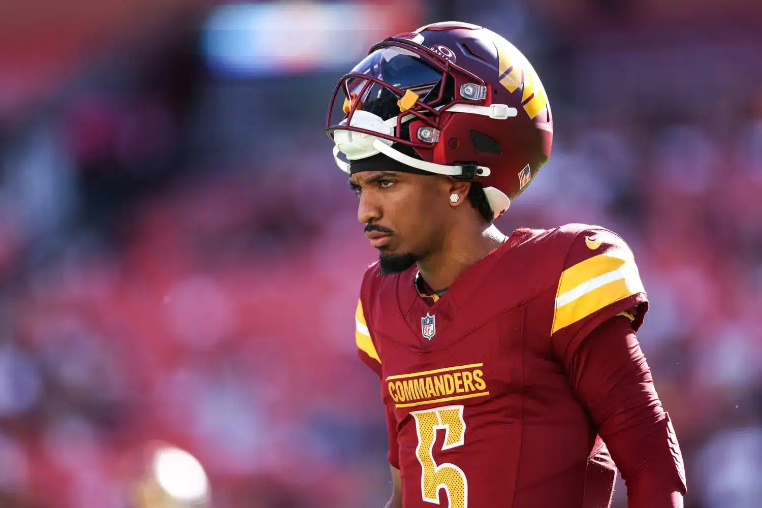 Jayden Daniels in Washington Commanders uniform with helmet on sidelines.