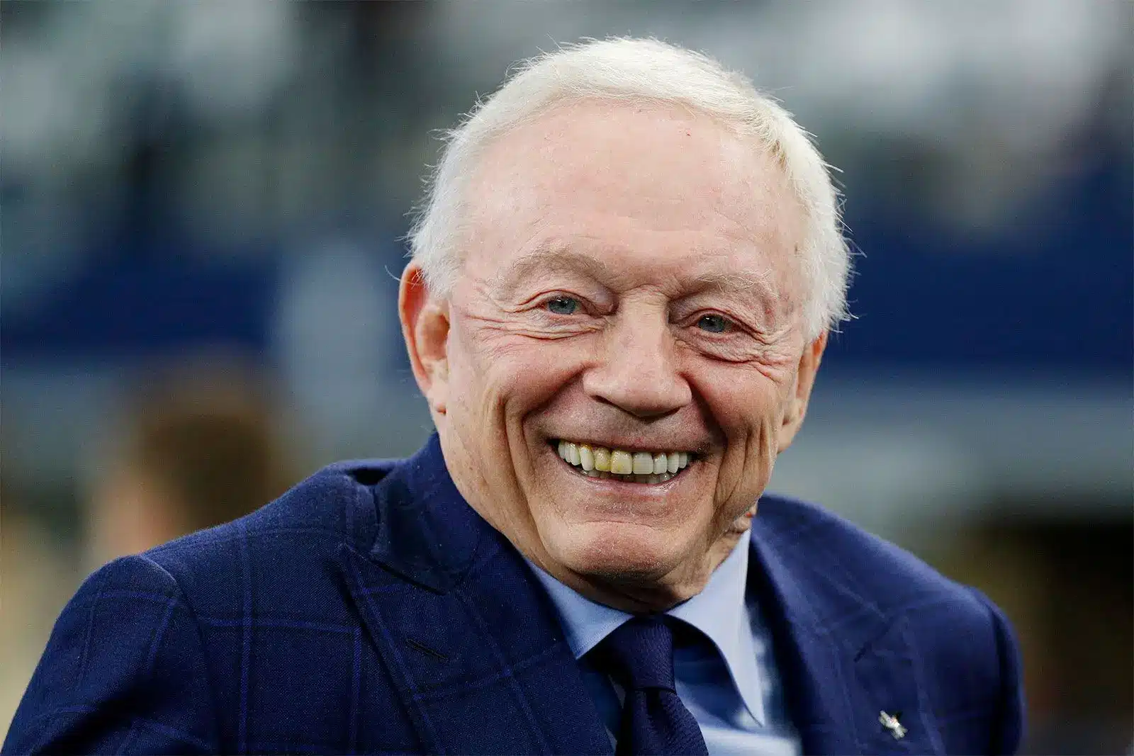 Close-up portrait of Jerry Jones smiling, wearing a navy blue patterned suit jacket and tie.