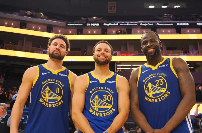 Klay Thompson, Stephen Curry, and Draymond Green posing together in blue Golden State Warriors jerseys