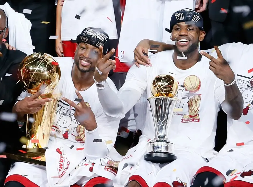 LeBron James and Dwyane Wade celebrating with NBA championship trophies and confetti.