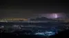 Lightning striking over Mexico City at night, illuminating the skyline and mountains.