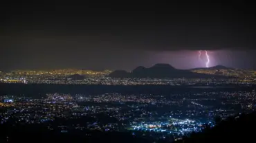 Lightning striking over Mexico City at night, illuminating the skyline and mountains.