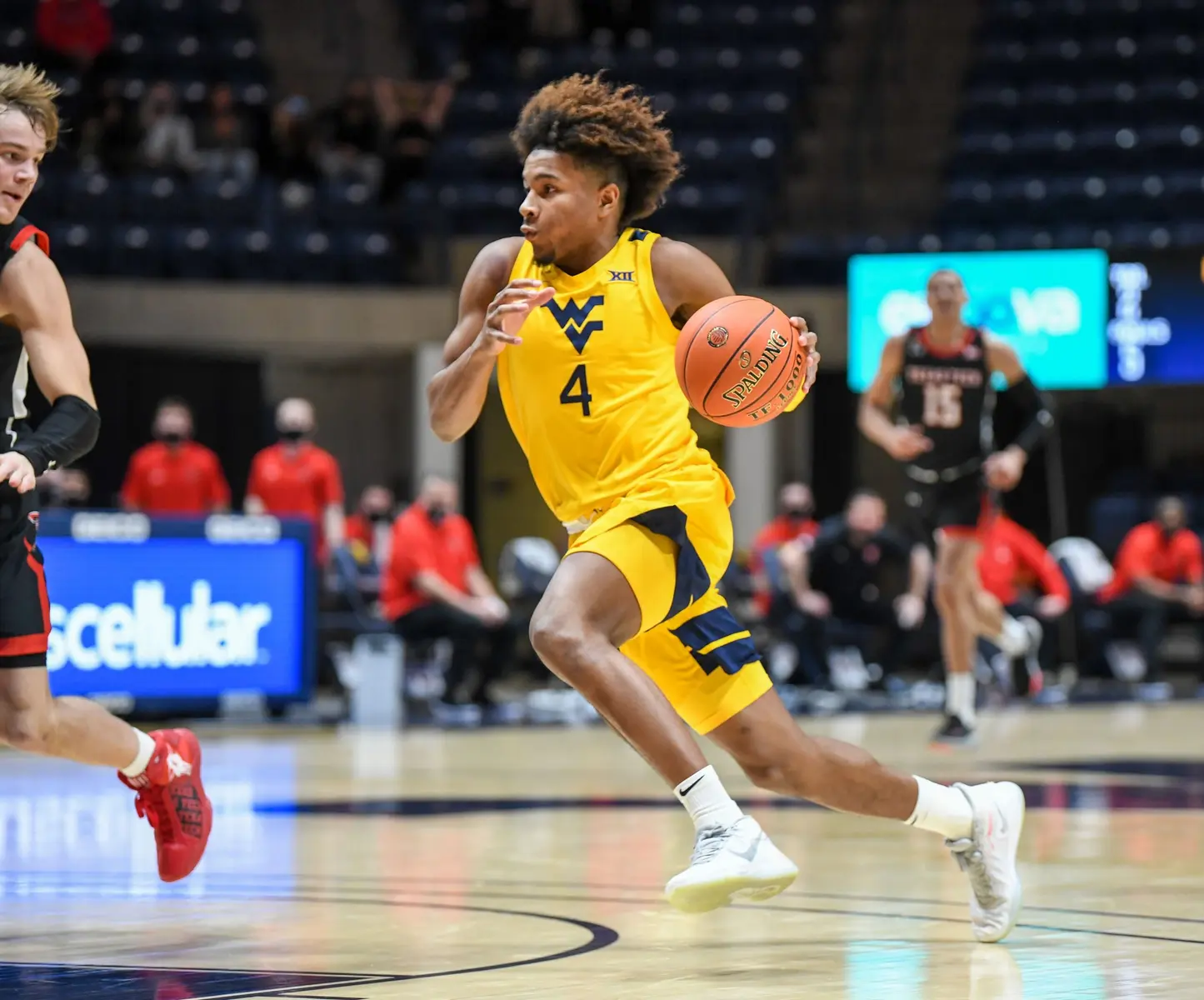 A basketball player in a yellow West Virginia jersey dribbles the ball during a game.
