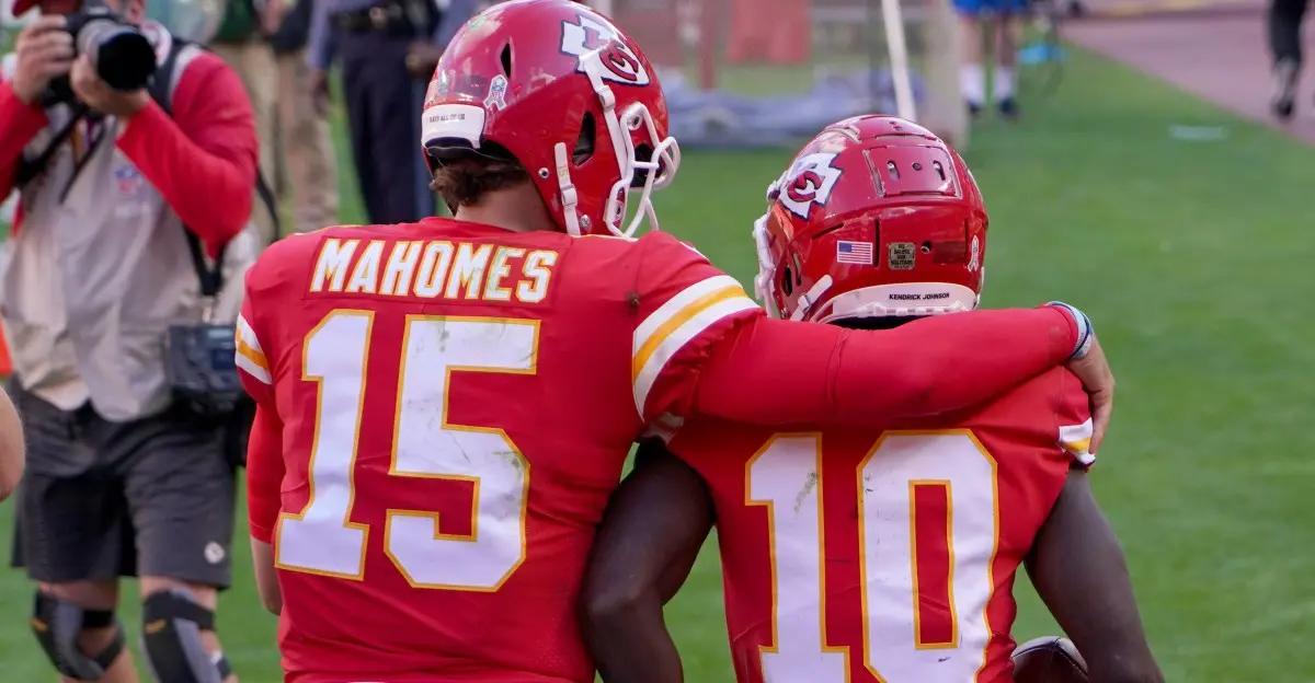 Patrick Mahomes and Tyreek Hill in Chiefs uniforms on the field embracing.