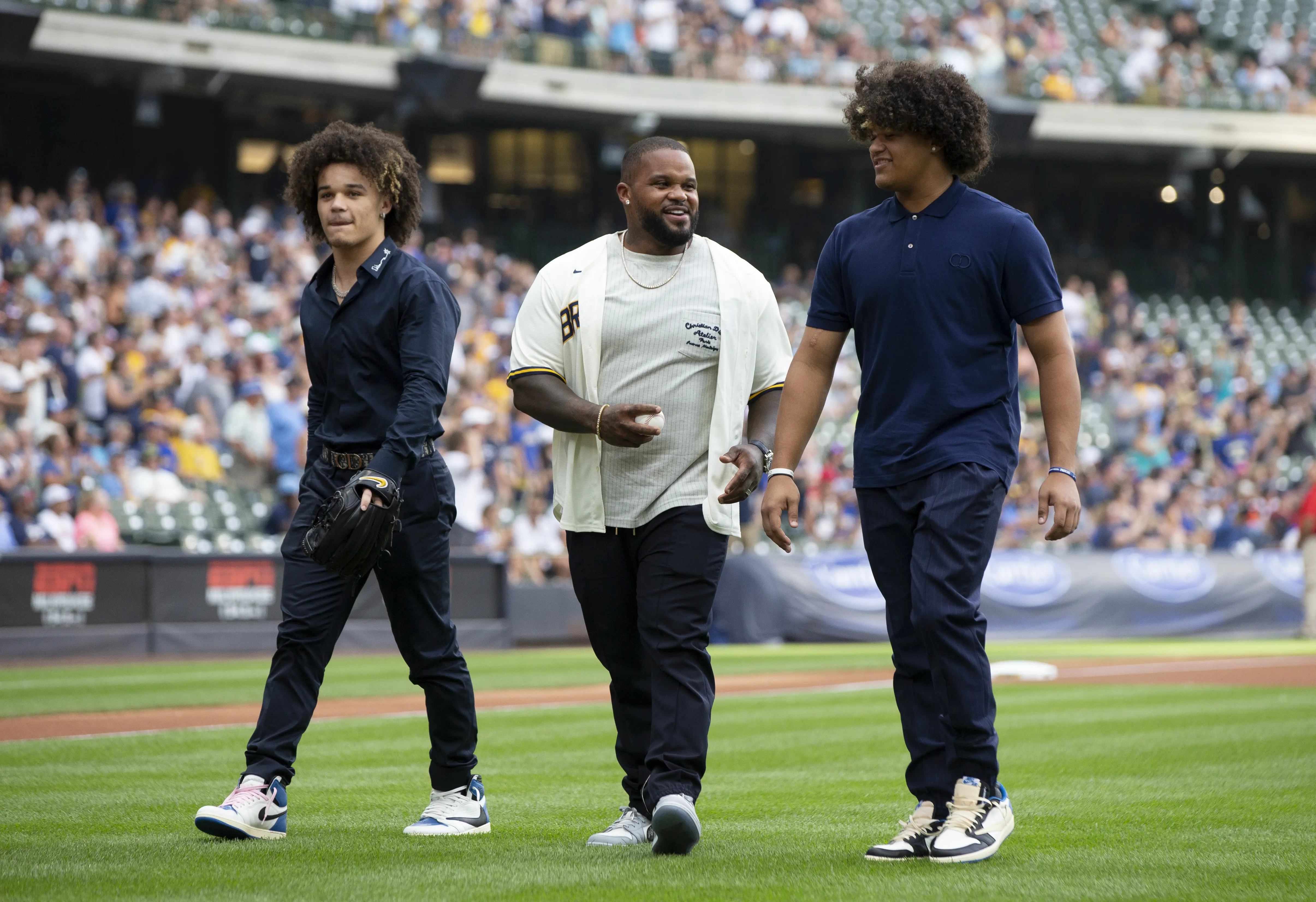 Prince Fielder and two young men walking on a baseball field during a game.