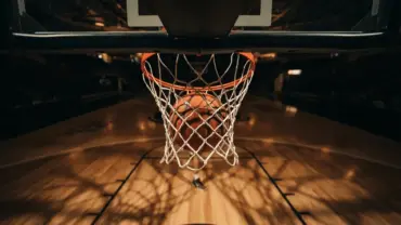 Basketball dropping through hoop net from below, dramatic sports photography lighting