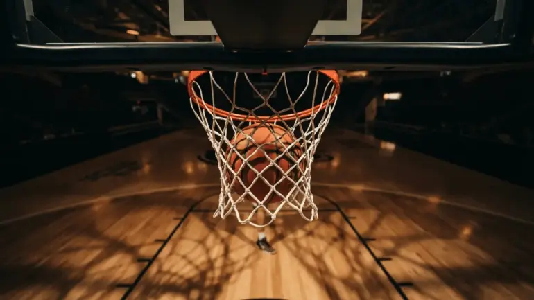 Basketball dropping through hoop net from below, dramatic sports photography lighting
