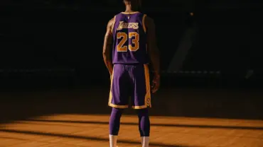LeBron James in Lakers jersey standing contemplatively on empty basketball court with dramatic lighting